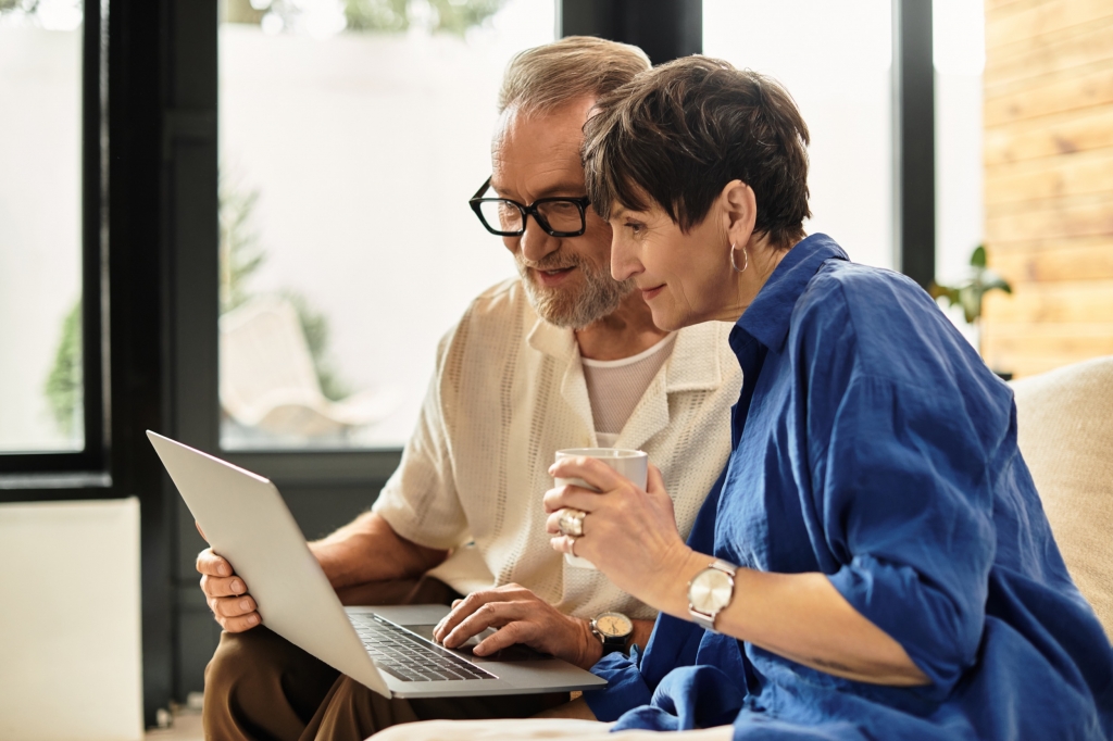A happy couple sits close, sharing a moment as they explore their laptop with coffee.